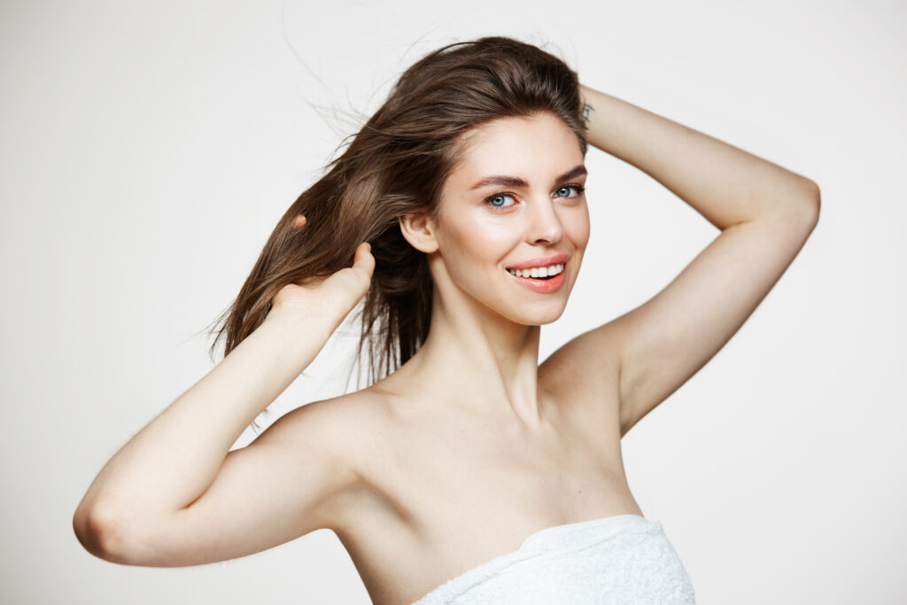 beautiful young woman with perfect clean skin smiling touching hair white wall facial treatment